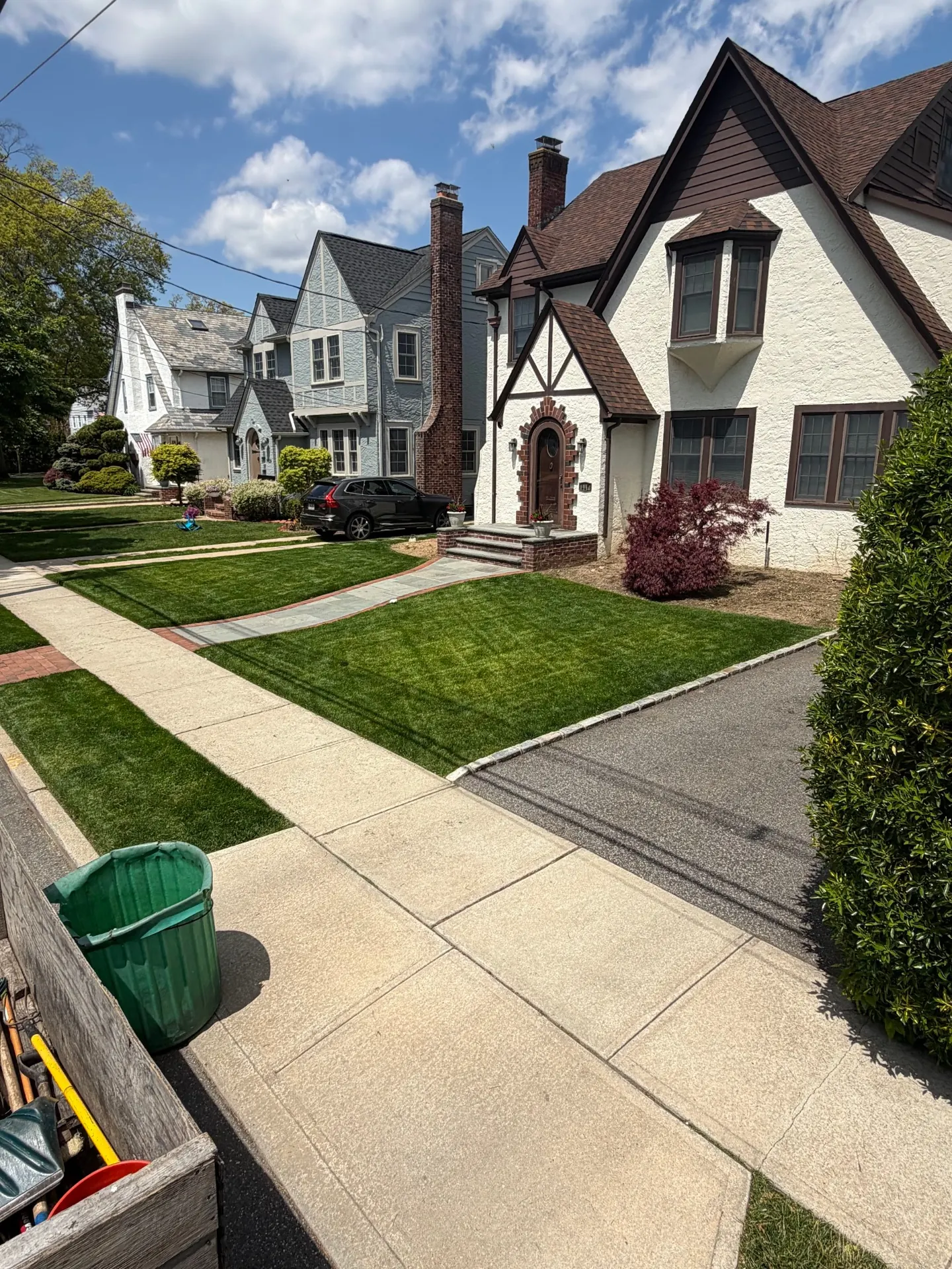 Manicured lawn and foundation plantings at a Tudor-style Long Island home by Greatness Landscaping & Construction